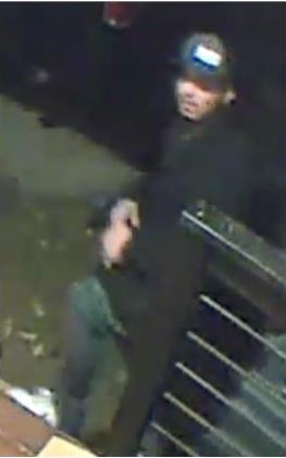 Camera footage photo of male suspect wearing a dark colored ball cap, black hoodie, dark jeans and white shoes.